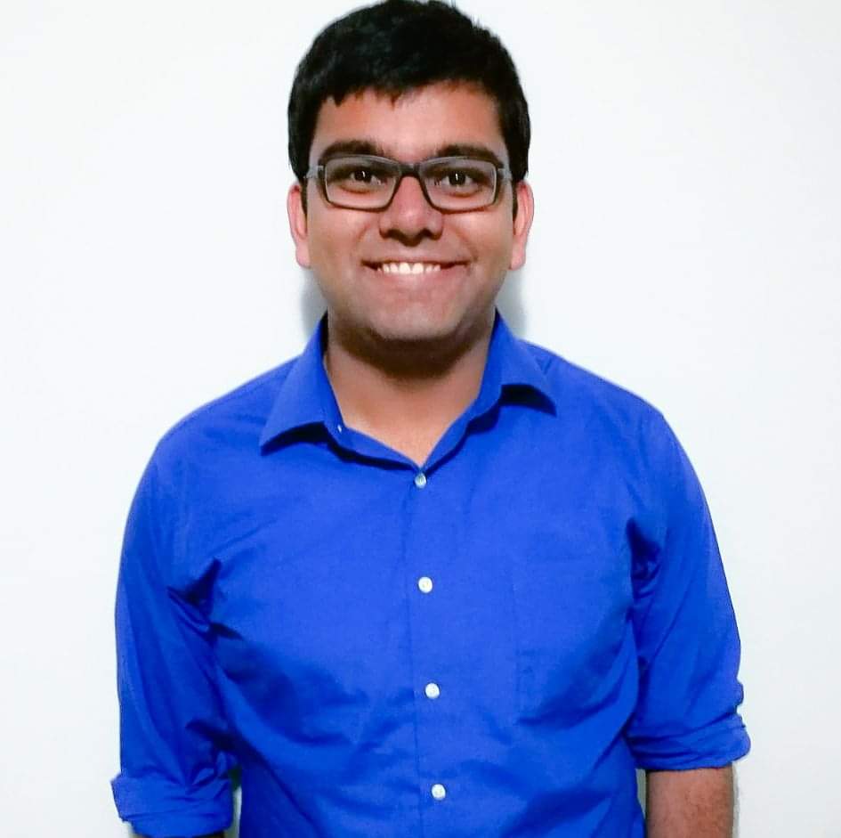 A medium skin toned man with short dark hair and glasses smiles against a white backdrop. His name is Armoghan and he is a member of the team.